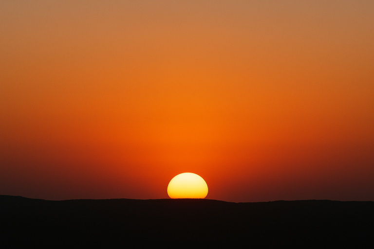 Bright yellow sun setting behind a dark hilly horizon.