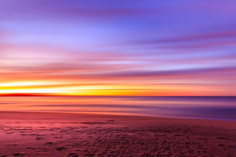 Vibrant long-exposure sunset at a beach with purple sky.